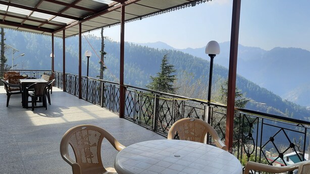 A covered terrace with a table and chairs, offering a view of a mountainous landscape. - Newly built bnb in a pristine village (Shimla)
