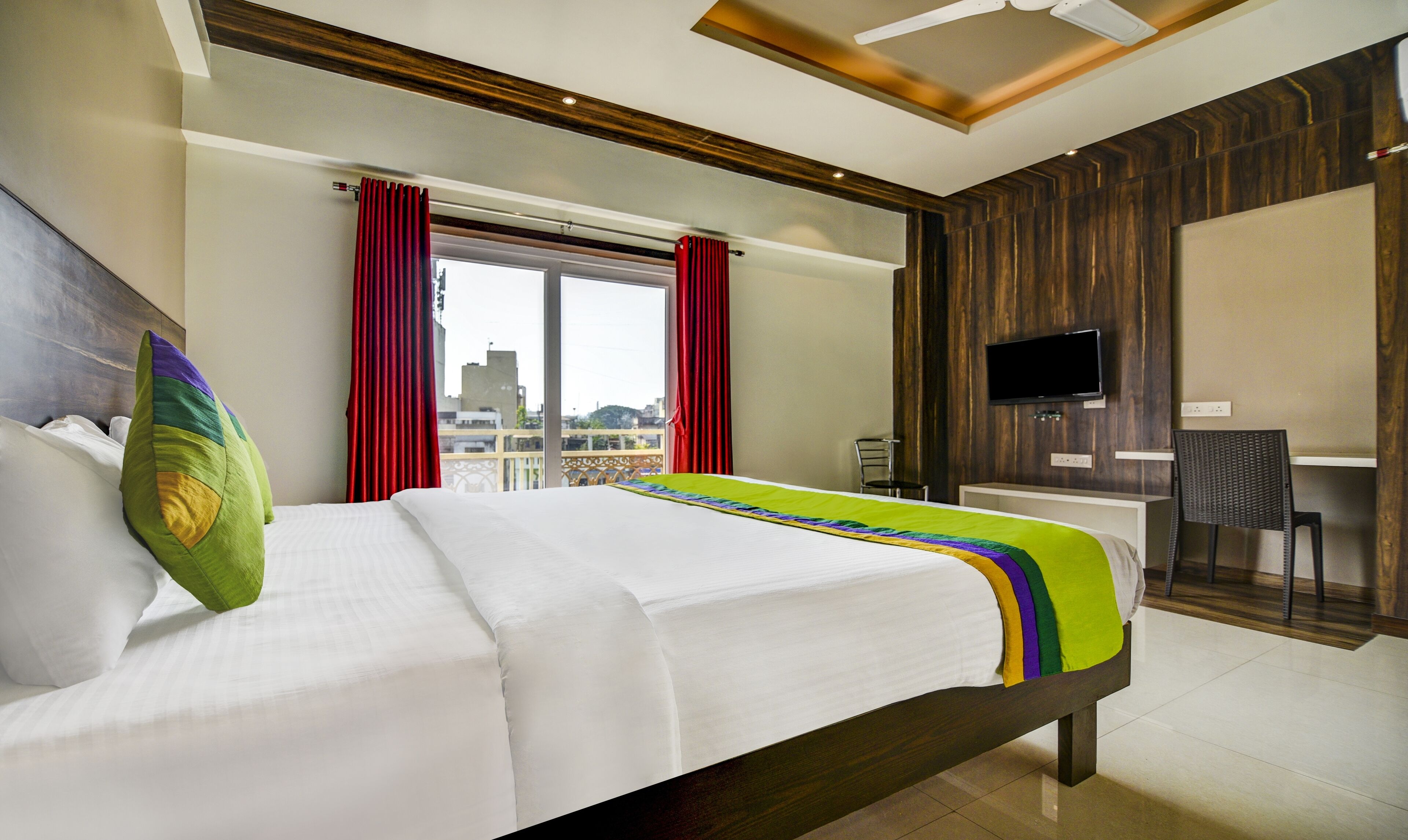 A hotel room with a large bed, a desk, a chair, a TV, and a window with curtains.