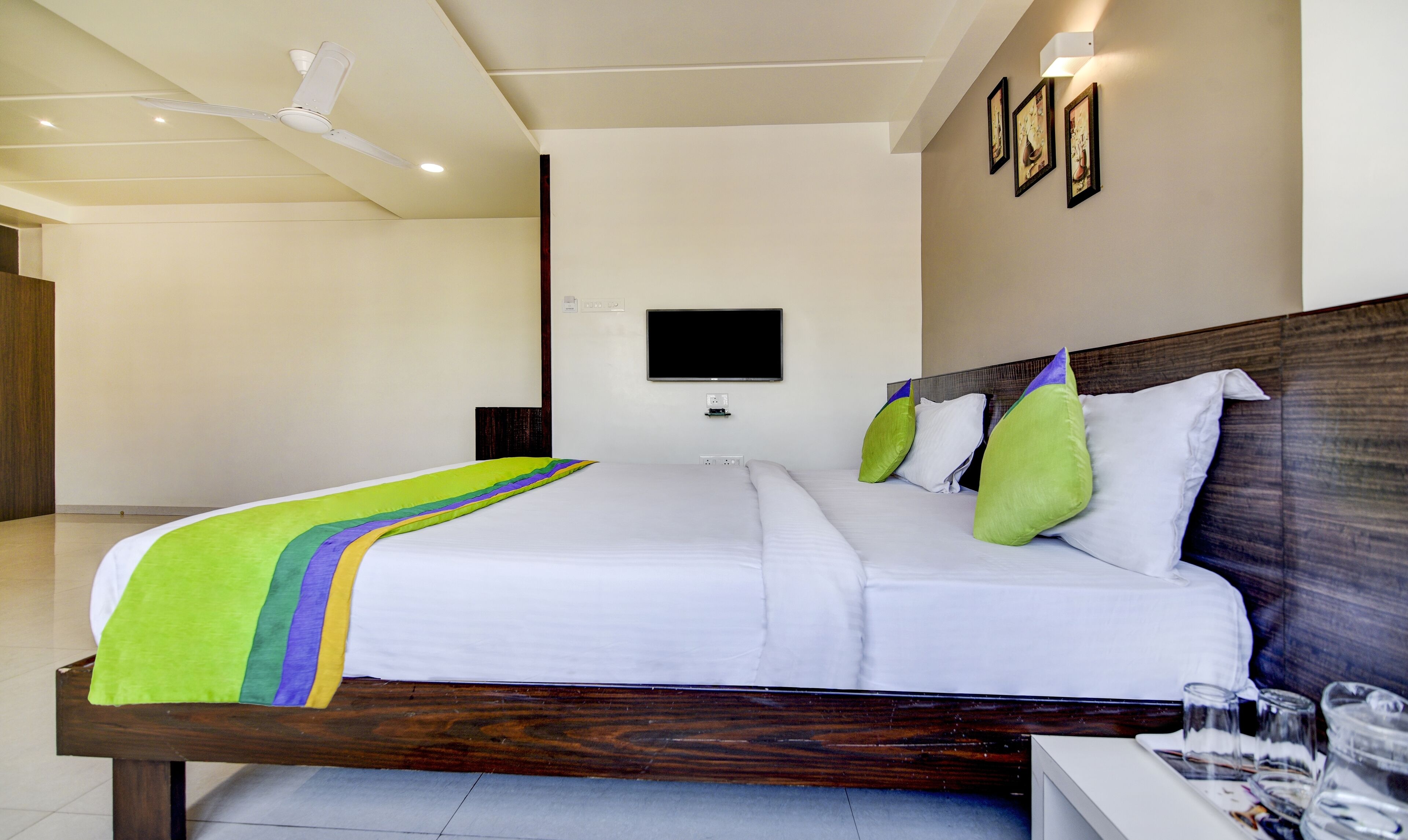 A hotel room with a large bed, a flat-screen TV mounted on the wall, and a ceiling fan.