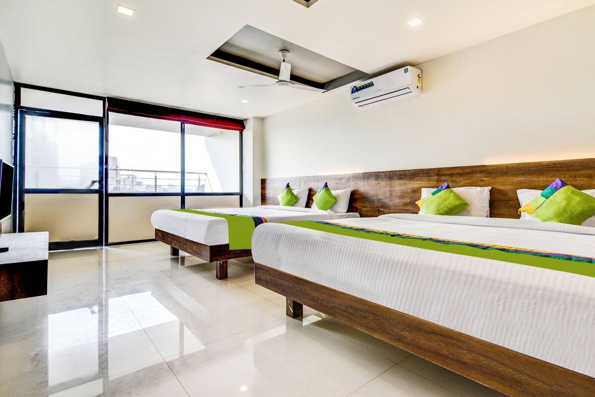 A hotel room with a large bed, a desk, and a window with blinds.