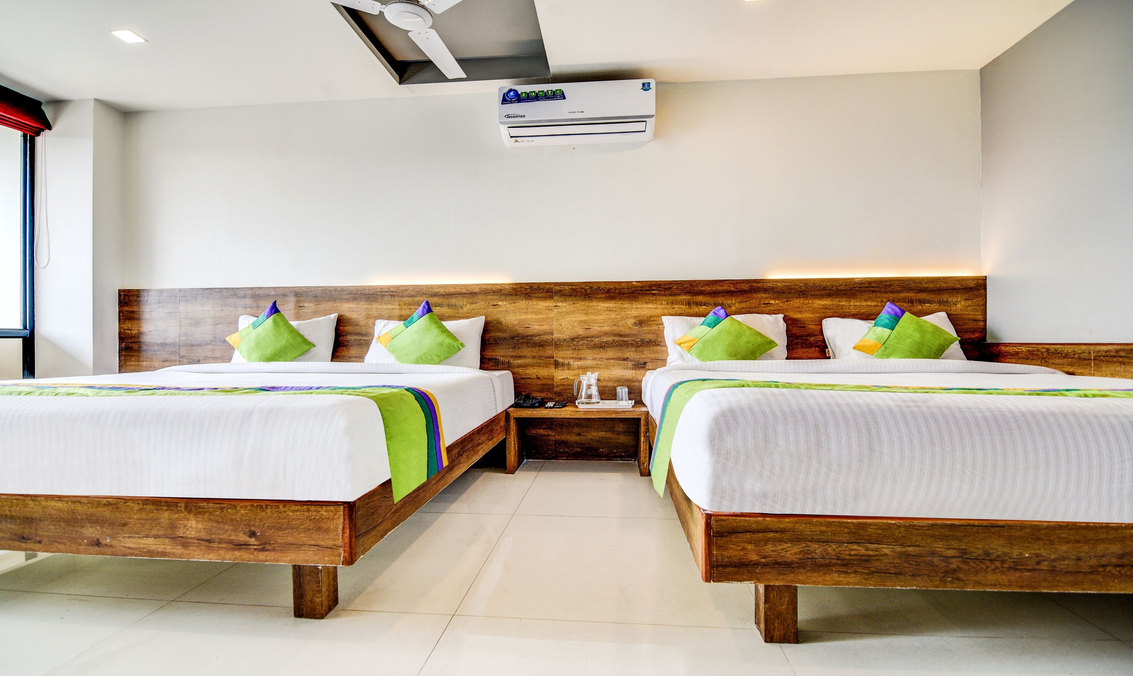 A hotel room with two beds, wooden headboards, white bedding, and a ceiling air conditioner.