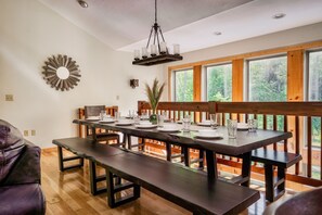 Un espace repas avec une longue table dressée pour six personnes, des bancs et un luminaire suspendu.