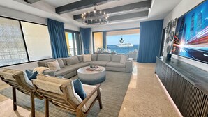Una sala moderna con un amplio sofá modular, una mesa de centro redonda y vistas al océano a través de grandes ventanales.