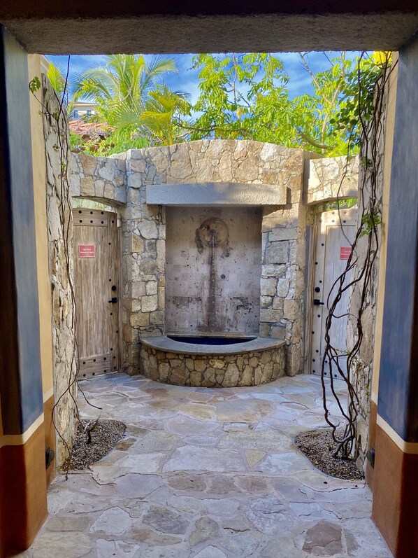 A stone-walled courtyard with a central water feature, surrounded by two wooden doors with signs.