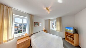 Hotellihuone, jossa on suuri sänky, puinen TV-taso, yöpöytä lampun kanssa ja ikkuna, jossa on verhot.