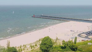 A beach with a pier extending into the water, a parking lot, and some greenery in the foreground. - 
Large Lakehouse w Private Beach~Hot Tub~Tiki Hut~Game Rm~Gym~Mini-Golf~Dogs OK! (Grand Junction)