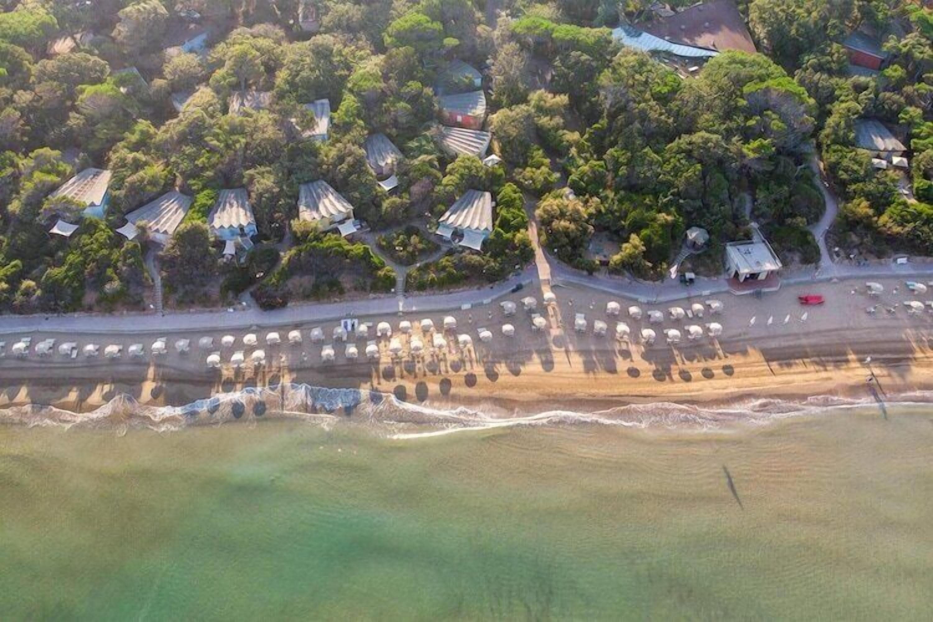 Luftaufnahme einer Küstenlandschaft mit mehreren Gebäuden, einer Straße und einem Strand.