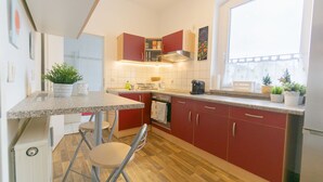 A compact kitchen with red cabinets, a granite countertop, a coffee maker, and a window with a view.
