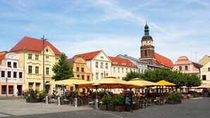 A square with outdoor seating, surrounded by historic buildings with red roofs and a prominent tower.