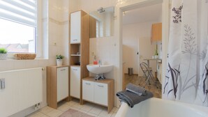 A modern bathroom with a white sink, wooden cabinets, a mirror, and a bathtub.