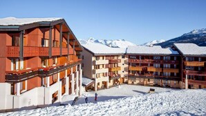 Ein Skigebiet mit mehrstöckigen Gebäuden, Skipisten und schneebedeckten Bergen im Hintergrund.