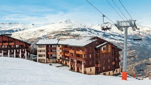 Un centro de esquí con edificios de varios pisos, telesillas y montañas nevadas al fondo.
