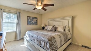 Un dormitorio con cama, ventilador de techo, ventana con cortinas, mesita de noche y un mapa del mundo en la pared.