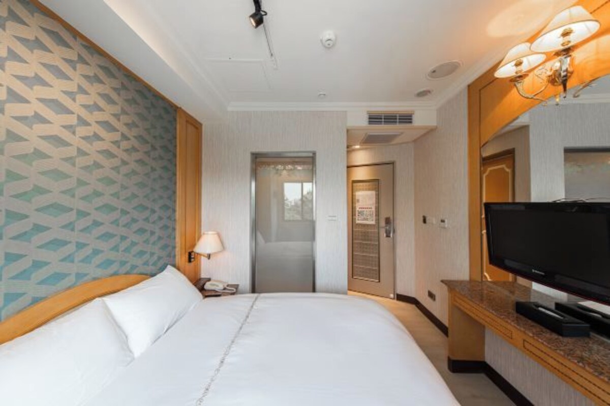 Ein Hotelzimmer mit Bett, Fernseher, Schreibtisch und einer Badezimmertür.