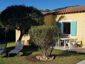Una casa con techo de tejas, un pequeño patio con mesa y sillas, y un árbol en el jardín.