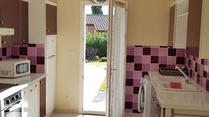Cocina compacta equipada con microondas, horno y lavadora. Una puerta da acceso a un jardín.