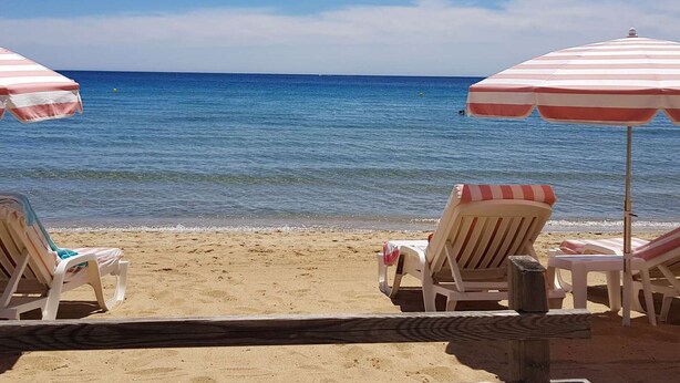 Una playa con dos sombrillas a rayas y sillas de playa.