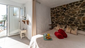 Una camera da letto con parete in pietra, un letto con cuscini rossi, un comodino con un vassoio per la colazione e una piccola finestra con tende.