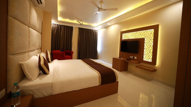 A modern hotel room with a large bed, a flat-screen TV, a ceiling fan, and a decorative wall panel.