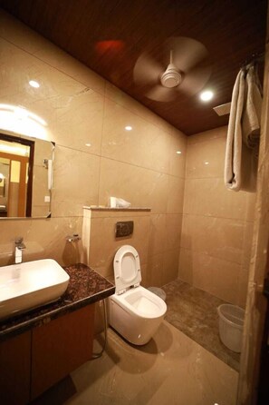 A bathroom with a marble vanity, a toilet, a ceiling fan, and a shower curtain. - Hotel Neerja Inn (Jaipur)