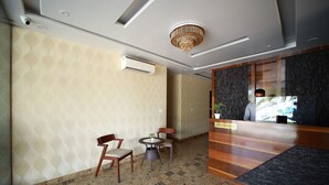 A hotel reception area with a modern design, featuring a reception desk, two chairs, a small table with a plant, patterned wallpaper, and a patterned floor.