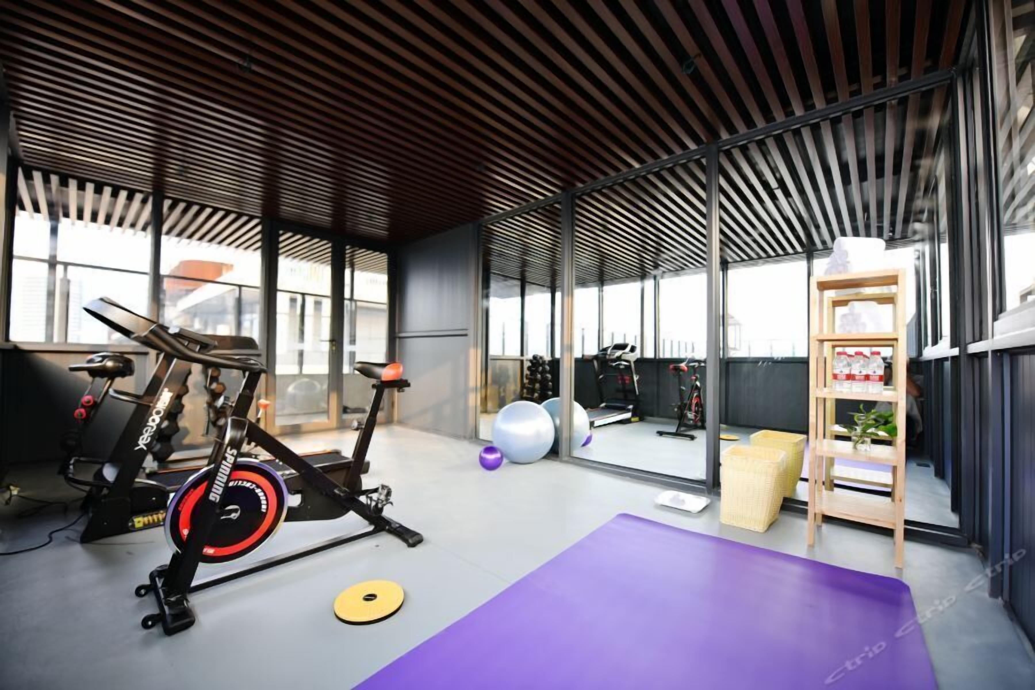 Une salle de sport moderne équipée de matériel d’exercice, avec un tapis violet et une étagère en bois où sont rangés divers objets.