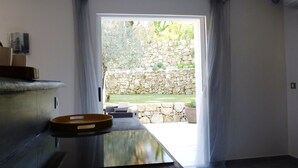 A modern kitchen with a large window, a stone wall outside, and a dining area with a table and chairs. - Superb house with heated pool in a beautiful garden (Le Rouret)