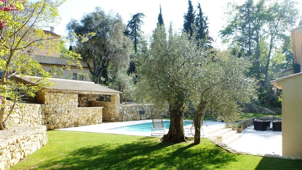 A stone house with a swimming pool, surrounded by lush greenery and tall trees. - Superb house with heated pool in a beautiful garden (Le Rouret)
