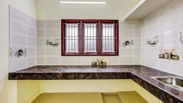 A kitchen with a marble countertop, a window with a red frame, and wall-mounted kitchen appliances. - HOTEL UMAIYYAL INTERNATIONAL (Nagercoil)