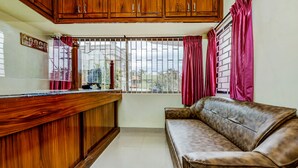 A room with a wooden counter, a sofa, and a window with metal bars and red curtains. - HOTEL UMAIYYAL INTERNATIONAL (Nagercoil)