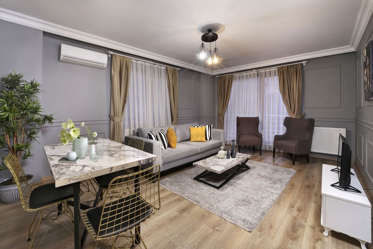 A modern living room with a marble coffee table, grey sofa, and a dining area with a marble table and chairs.
