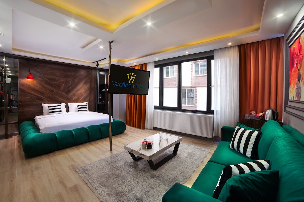 A modern hotel room with a bed, green sofa, and a TV displaying the hotel name.