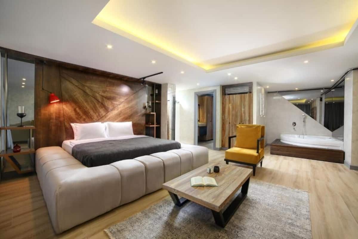 A modern bedroom with a bed, a sofa, a chair, and a small table. There is a staircase leading to an upper level.