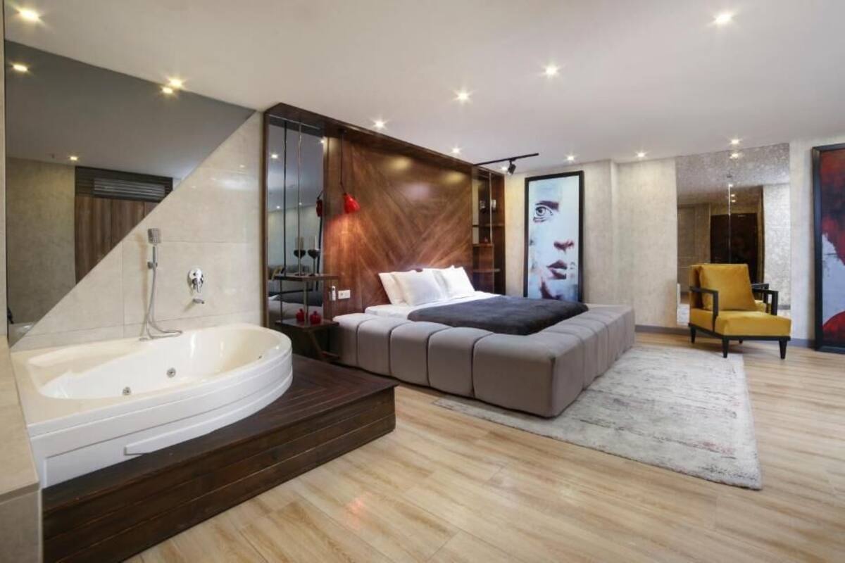 A modern bedroom with a large bed, a bathtub, and a chair.