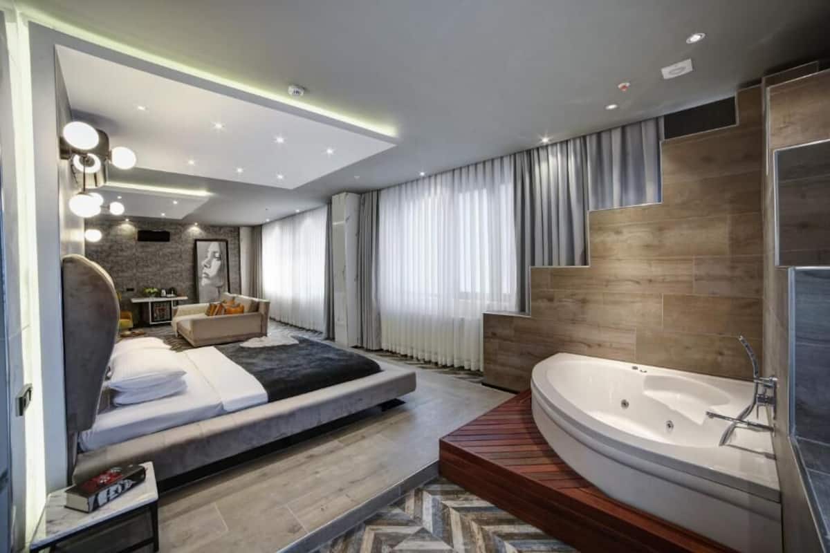 A modern bedroom with a large bed, a built-in desk, a vanity with a mirror, and a walk-in shower.