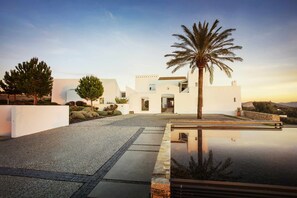 Un edificio moderno y blanco con una piscina reflectante y palmeras.