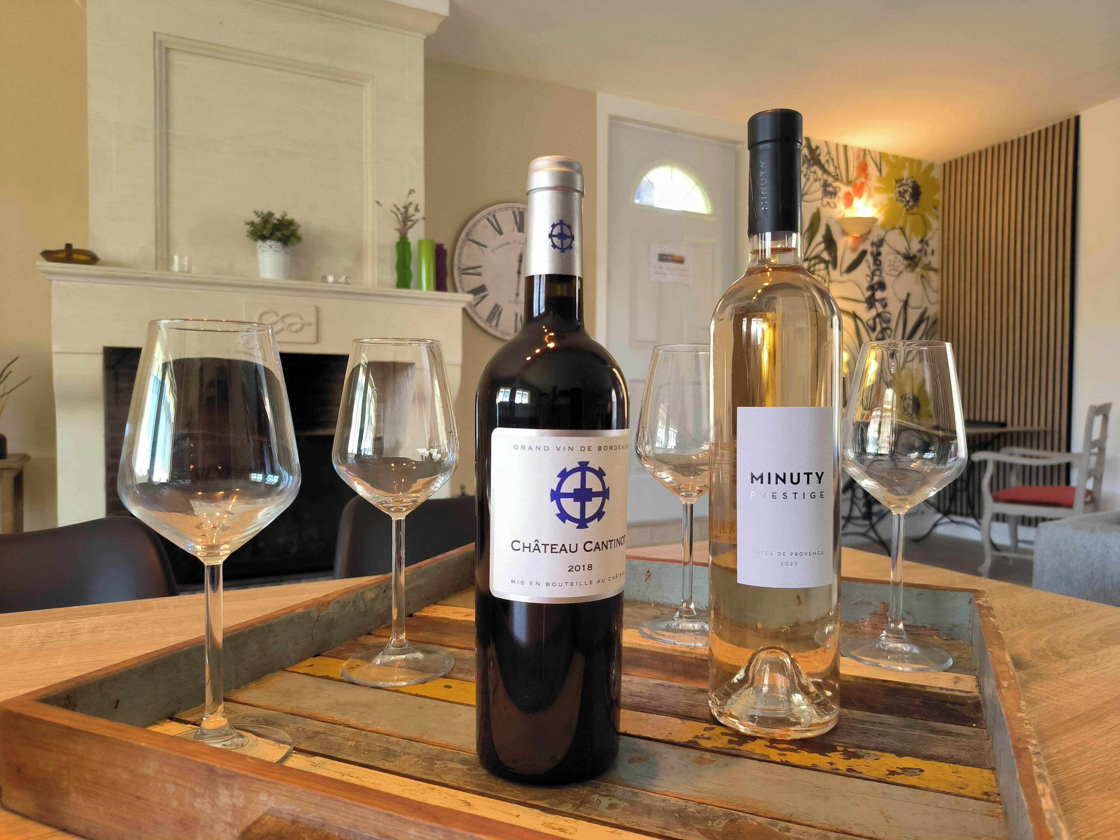 A wooden table with three wine glasses and two bottles of wine.
