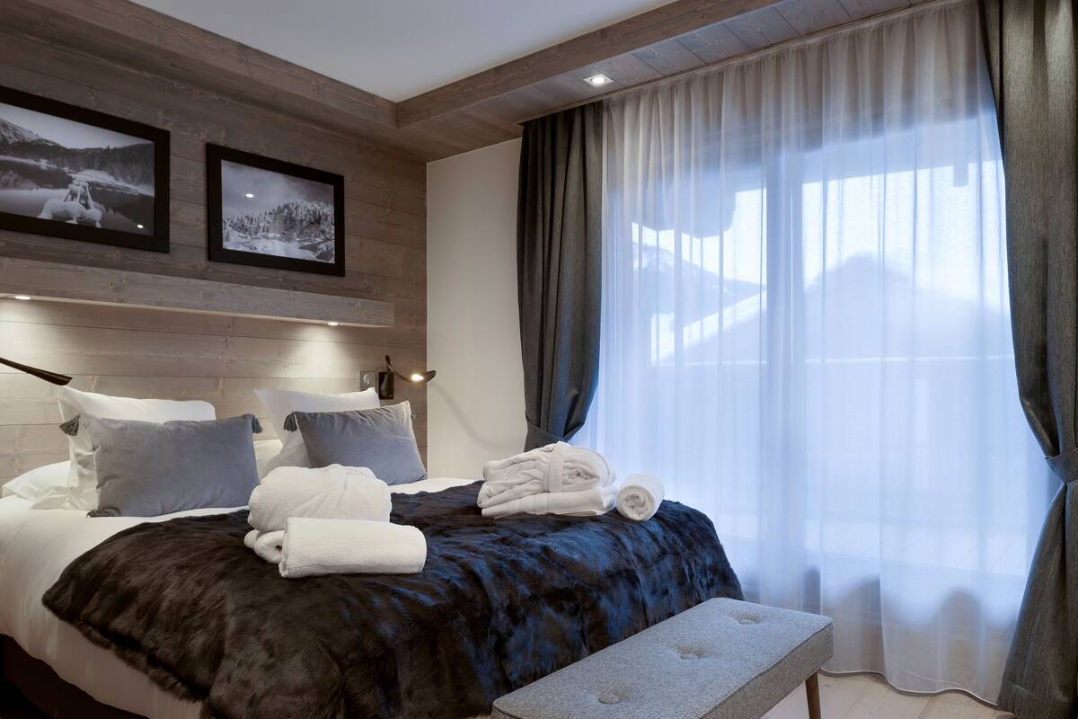 Ein modernes Hotelzimmer mit einem großen Bett, dunkelblauer Bettwäsche und zwei gerahmten Fotografien an der Wand.