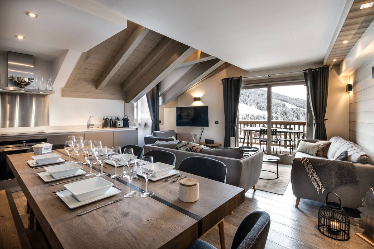Eine moderne Küche mit Holzbalkendecke, ein Essbereich mit einem langen Tisch für sechs Personen und eine gemütliche Wohnbereich mit einer Couch und einem Fernseher.