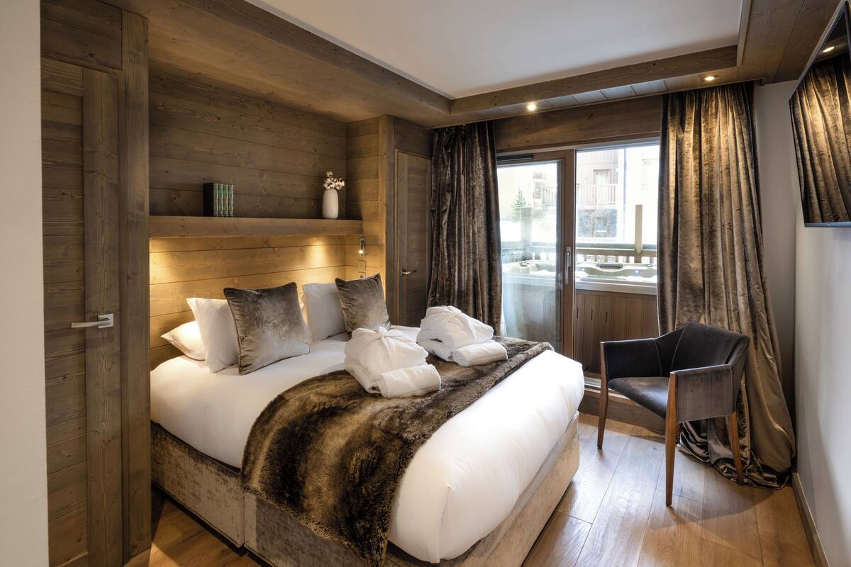 Ein Schlafzimmer mit einem großen Bett, einem Holzkopfteil, einem Sessel und Blick ins Freie.