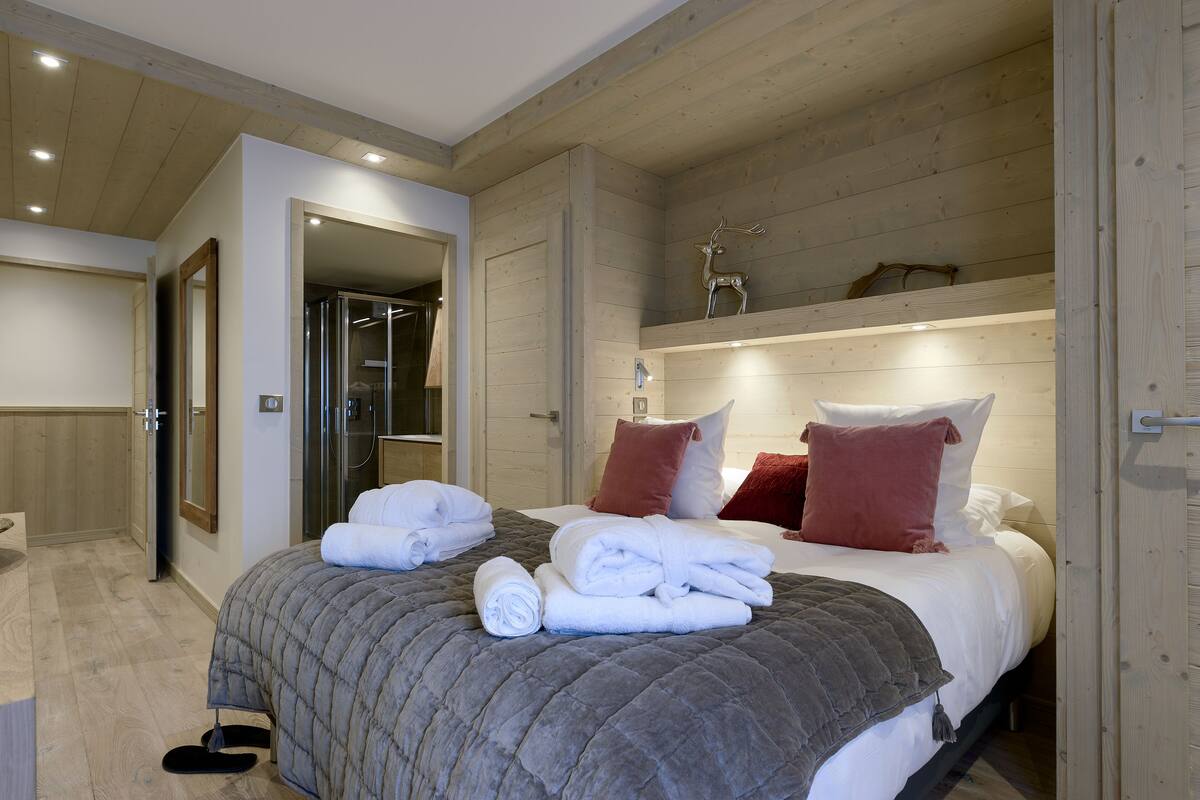 Ein Schlafzimmer mit Bett, Handtüchern, Holzboden und Spiegel.