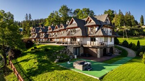 Fileira de edifícios no estilo chalé, com varandas, situada numa encosta com um jardim bem cuidado e uma área de piscina pequena.
