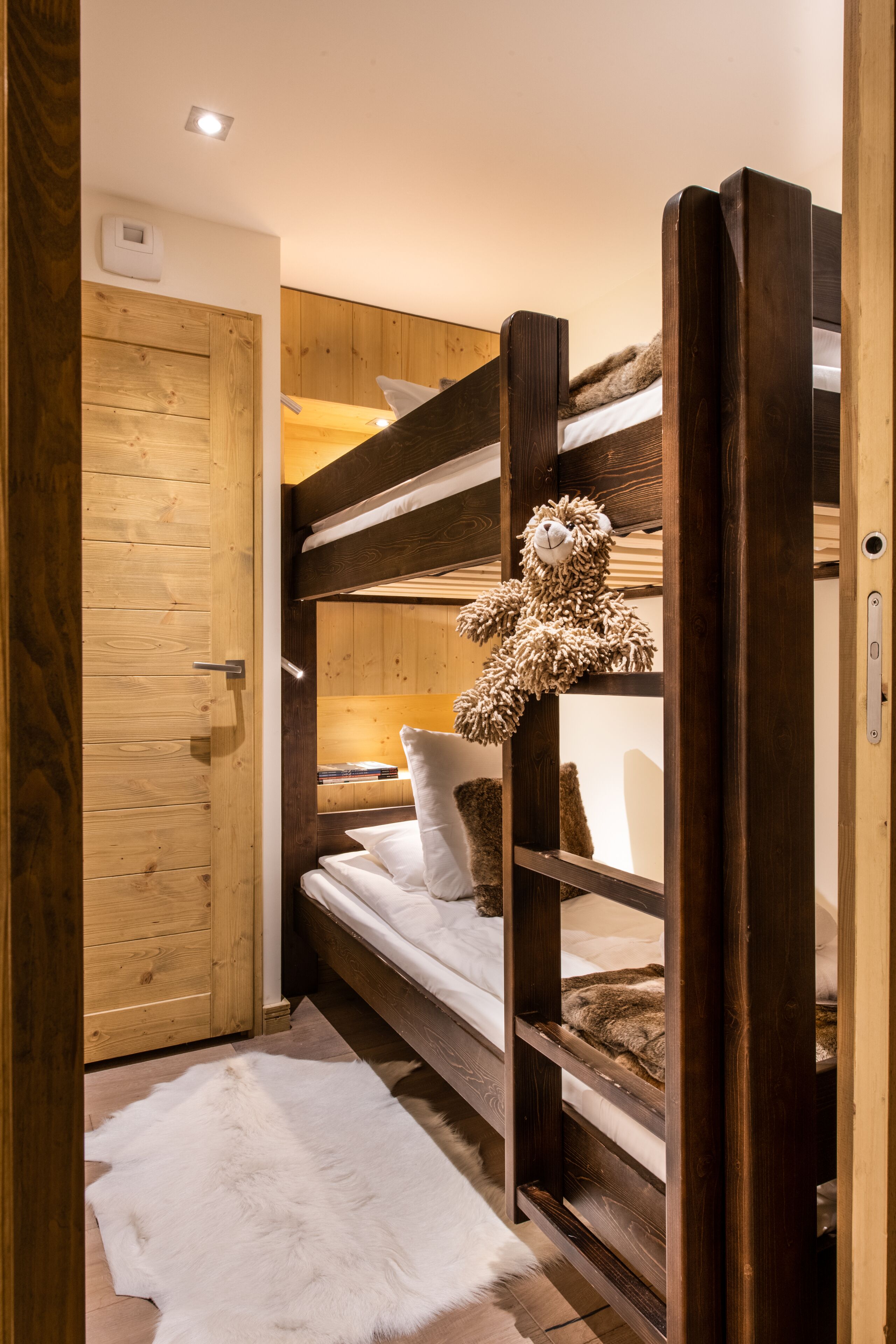 A bunk bed with a teddy bear, a wooden door, and a white fur rug.