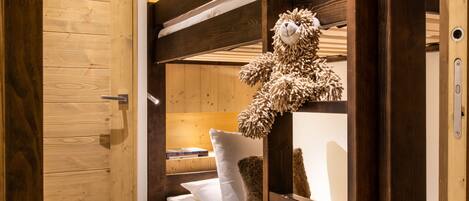 A bunk bed with a teddy bear, a wooden door, and a white fur rug.