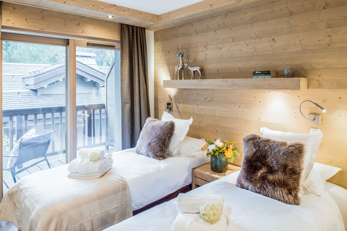 Ein Hotelzimmer mit zwei Betten, Holzboden, einem Balkon mit Blick und einem Regal mit Dekoration.