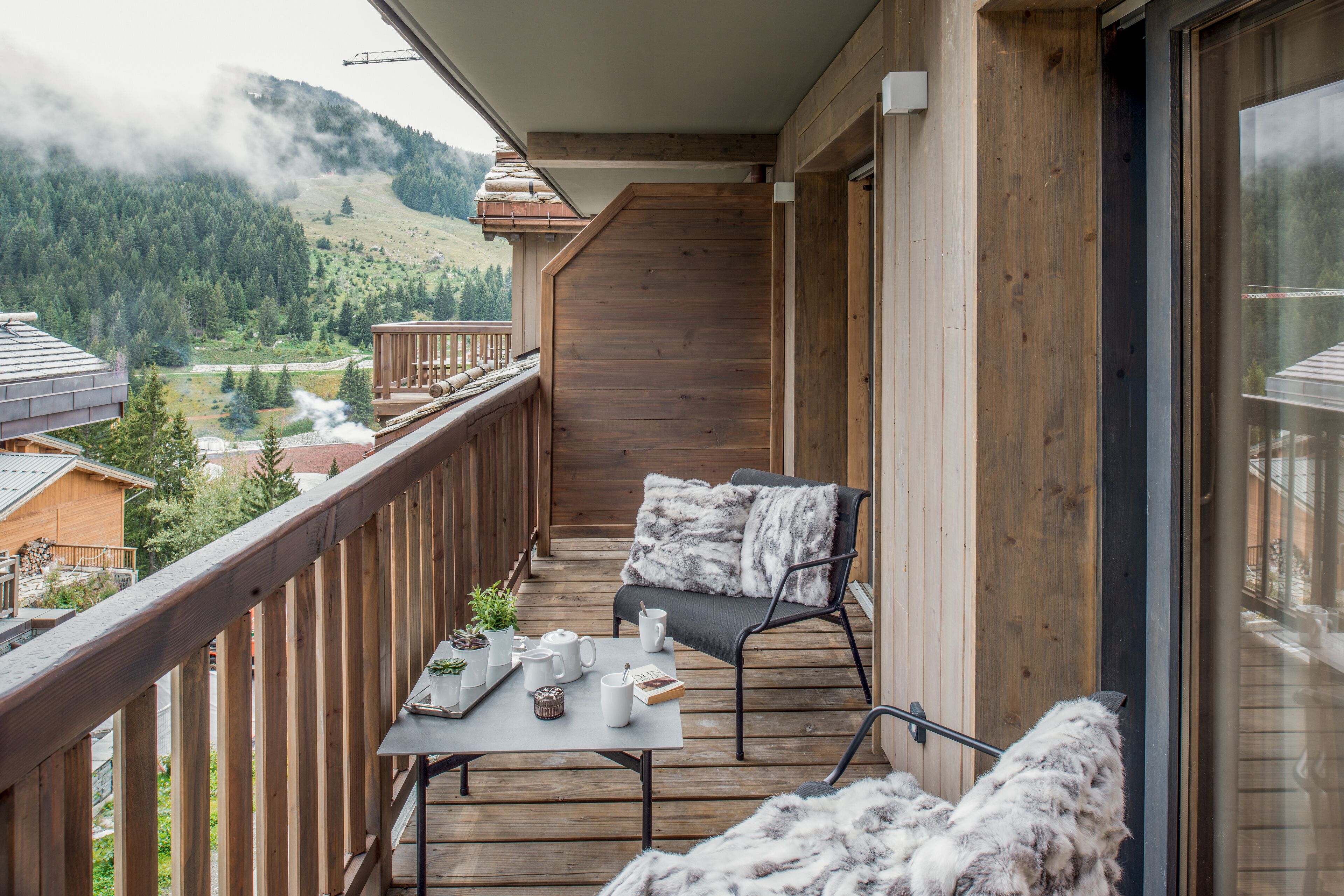Een balkon met een houten hekwerk, een tafel met een stoel, en uitzicht op een bergachtig landschap.