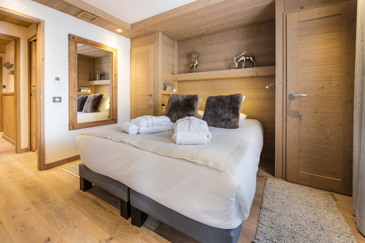 Ein modernes Schlafzimmer mit einem großen Bett, Holzwänden, einer eingebauten Ablage mit Dekoration und einem Spiegel über dem Bett.