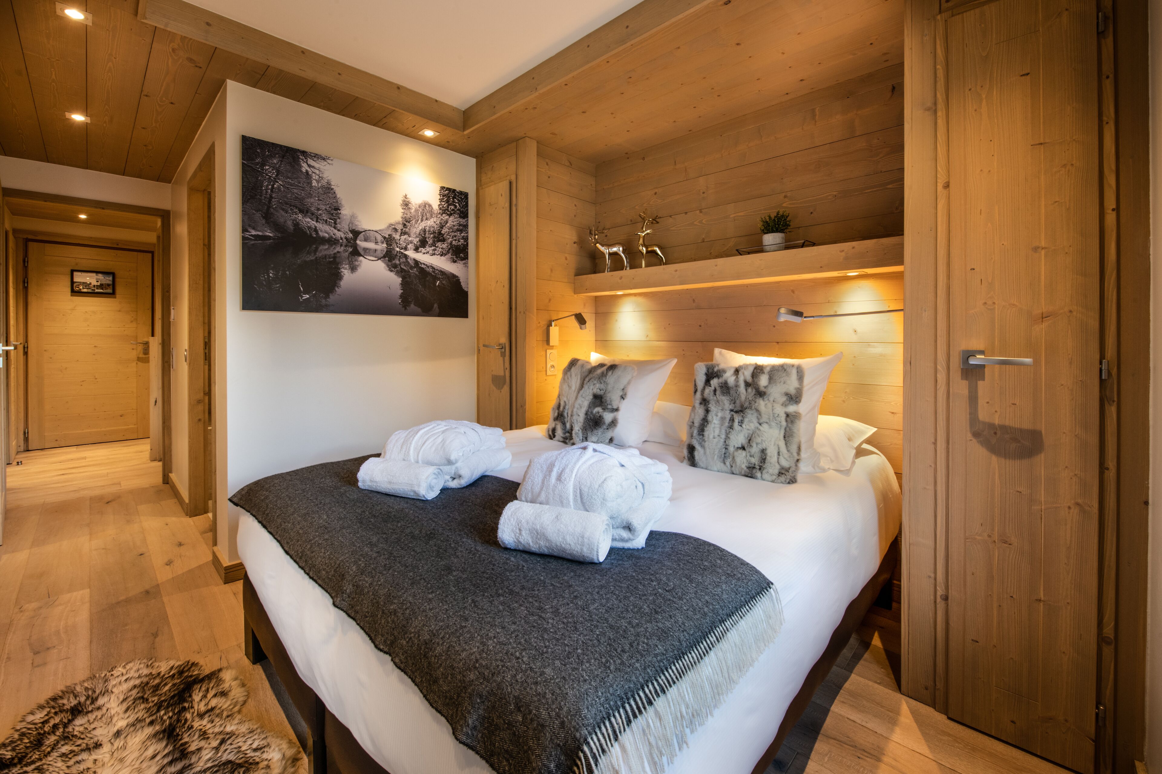 Dormitorio con paneles de madera, una cama, toallas, una fotografía en la pared y una estantería con adornos.