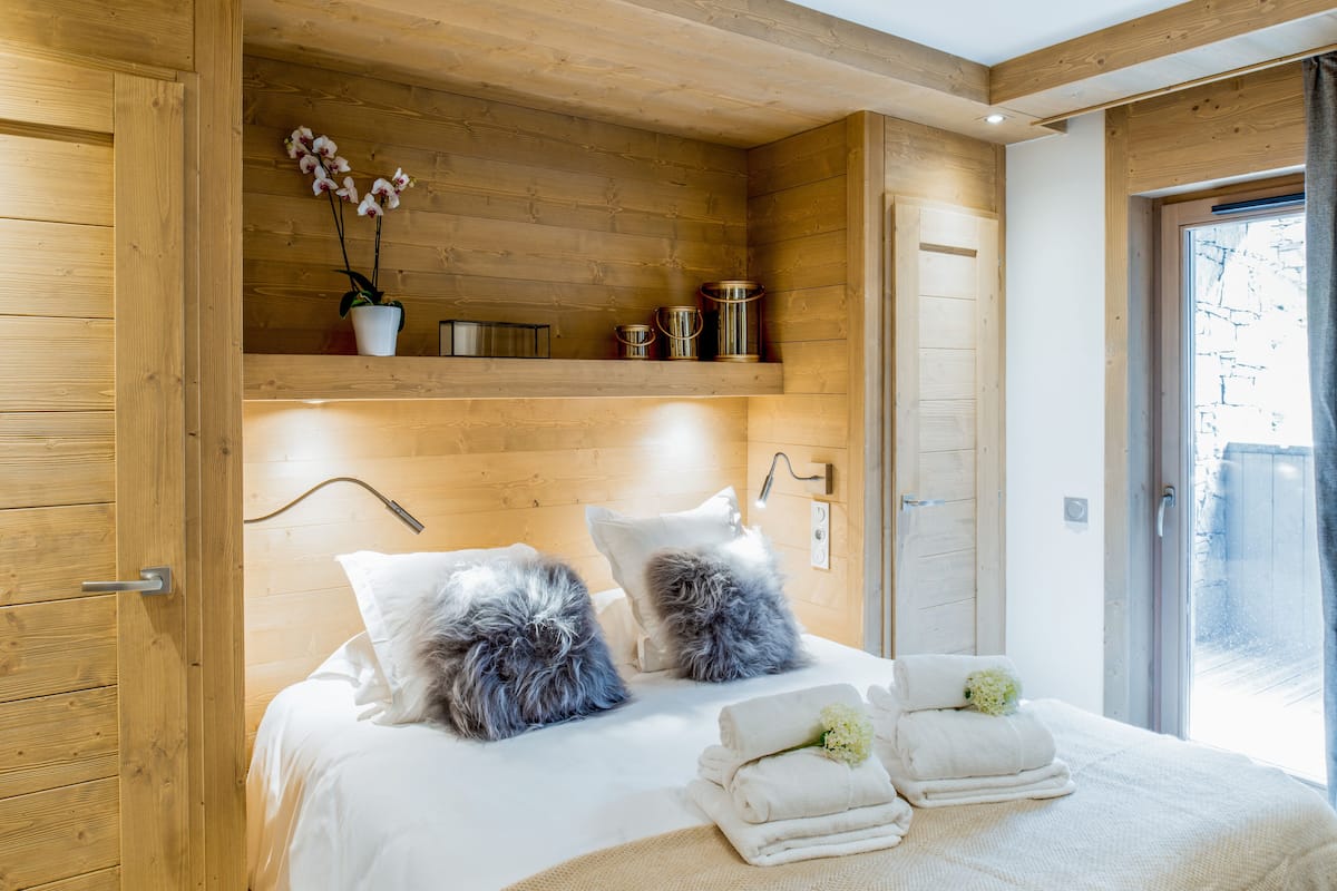 Ein Schlafzimmer mit Holzwänden, einem Bett, Kissen, einem Nachttisch und einem Fenster.