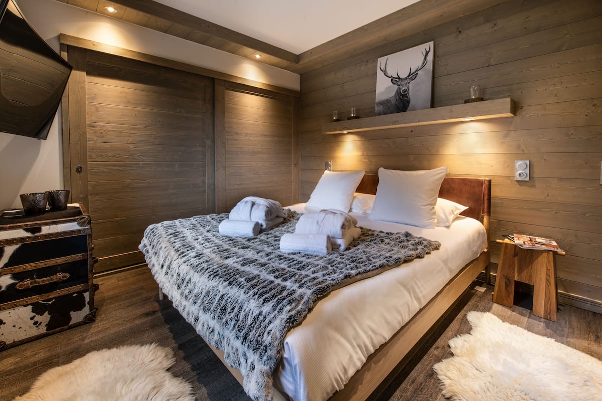 Ein schlafgemach mit Holzwänden, einem Bett, einer Holzkiste und einem aufgehängten Bild eines Rehs.
